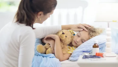 Kranker kleiner Junge mit Asthma-Medikamenten. Mutter mit krankem Kind liegt im Bett. Ungesundes Kind mit Kammerinhalator zur Hustenbehandlung. Grippesaison. Elternteil im Schlafzimmer oder Krankenhauszimmer für junge Patienten.