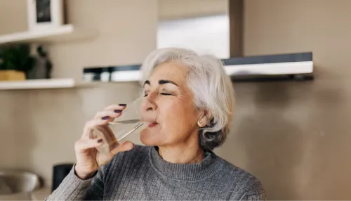 Ältere Frau trinkt frisches Leitungswasser aus einem Glas.