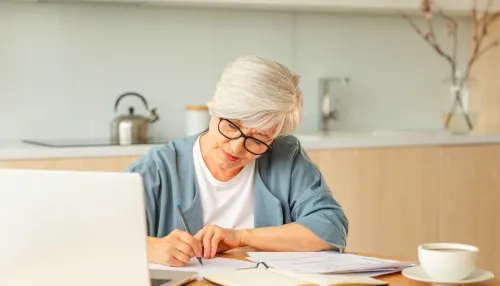 Seniorin mittleren Alters mit Laptop und Notizen zu Hause.