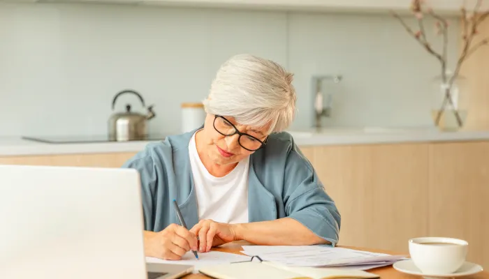 Seniorin mittleren Alters mit Laptop und Notizen zu Hause.
