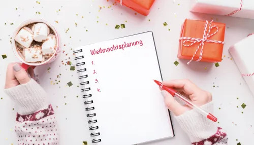Person die auf einem weihnachtlich dekorierten Tisch eine Checkliste in ein Heft schreibt.