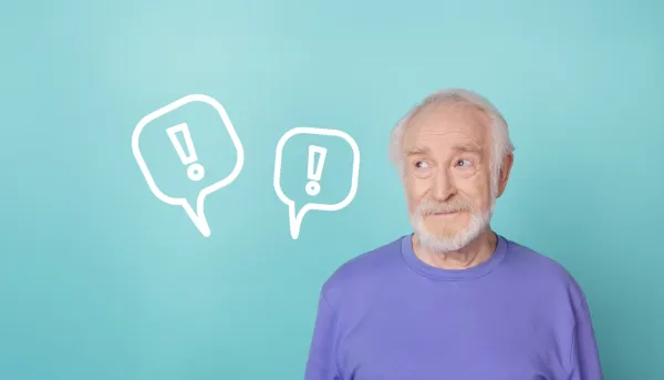 Älterer Mann auf einem türkis-farbenen Hintergrund der auf zwei Ausrufezeichen in Sprechblasen schaut