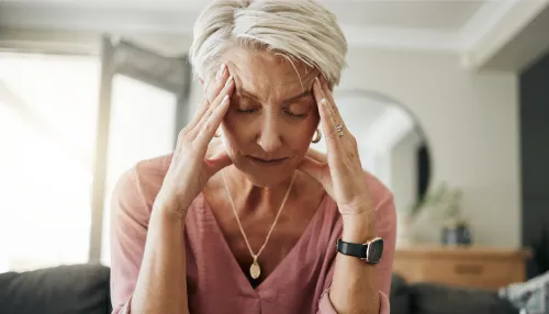 Ältere Frau mit Kopfschmerzen, Stress und Depressionen, während sie sich müde, ausgebrannt und ängstlich auf dem Sofa zu Hause fühlt.