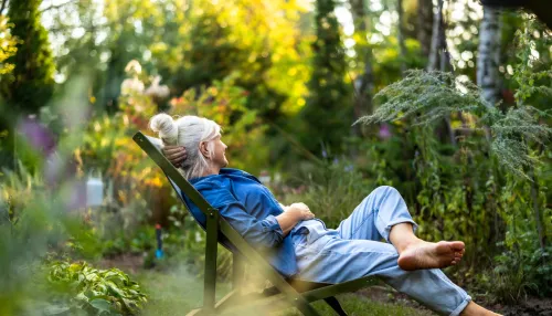 Ältere Frau, die sich in ihrem Garten im Liegestuhl entspannt