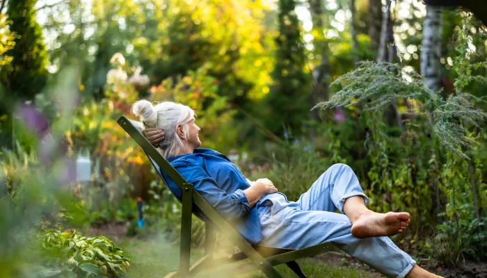 Ältere Frau, die sich in ihrem Garten im Liegestuhl entspannt
