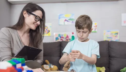 Kinderpsychologin mit spielendem Kind in einem gemütlich eingerichtetem Zimmer mit Kinderbildern und Spielzeug