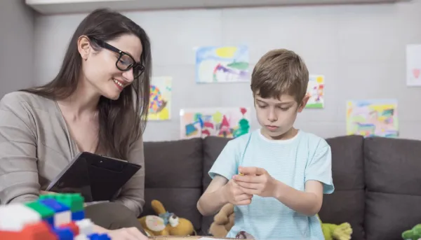 Kinderpsychologin mit spielendem Kind in einem gemütlich eingerichtetem Zimmer mit Kinderbildern und Spielzeug