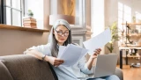 Ältere Frau arbeiten beschäftigt zu Hause mit Laptop und begutachtet Unterlagen