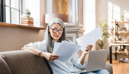 Ältere Frau arbeiten beschäftigt zu Hause mit Laptop und begutachtet Unterlagen