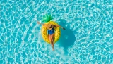 Frau im Urlaub allein in einem Swimmingpool auf einer Ananas Luftmatratze treibend
