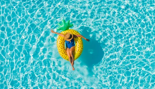 Frau im Urlaub allein in einem Swimmingpool auf einer Ananas Luftmatratze treibend