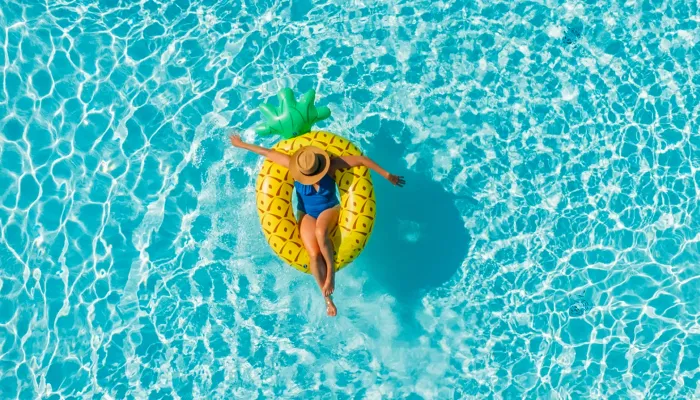 Frau im Urlaub allein in einem Swimmingpool auf einer Ananas Luftmatratze treibend