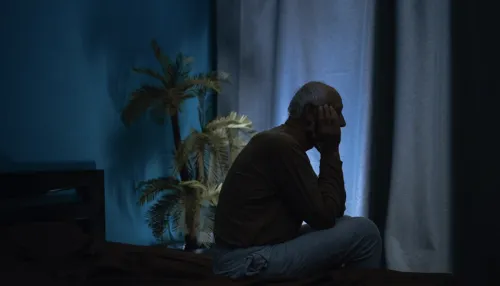 Silhouette eines alten Mannes, der an Schlaflosigkeit leidet und nachts schläfrig auf dem Bett sitzt.