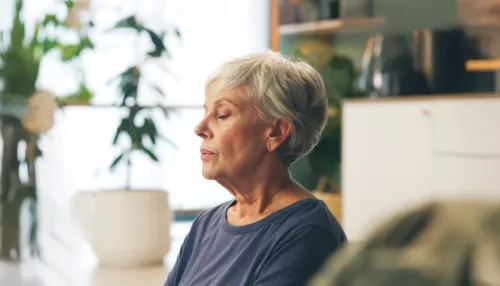 Seniorin meditiert in ihrem Wohnzimmer