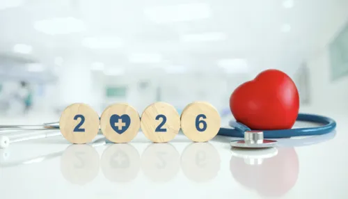 Stethoskop und rotes Herz neben runden Holzscheiben, die das Jahr 2026 in einem hellen Krankenhaus zeigen.